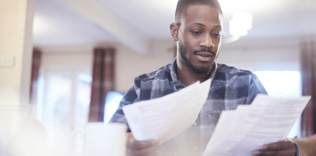 Photo of a male in a black checkered button-up shirt intently reading a contract. He appears focused and engaged, with his eyes fixed on the text in front of him.