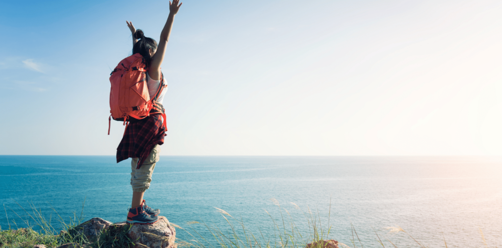 A confident woman embracing adventure, wearing a backpack and exploring a scenic outdoor location during her travel nurse assignment's downtime. She radiates joy as she takes in the beauty of her surroundings, ready to seize every opportunity to make lasting memories on her journey.
