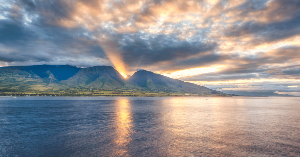 Amidst the aftermath of the devastating Maui wildfires, a serene sunrise paints the sky with delicate shades of orange and pink over the island's horizon, symbolizing hope and resilience in the face of adversity.